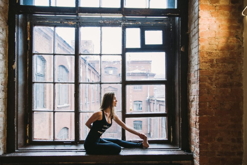 Una donna fa stretching seduta davanti a una grande finestra