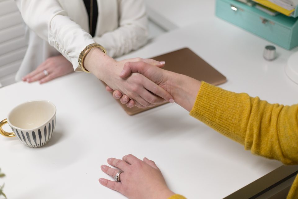 Due persone si stringono la mano sopra un tavolo con documenti