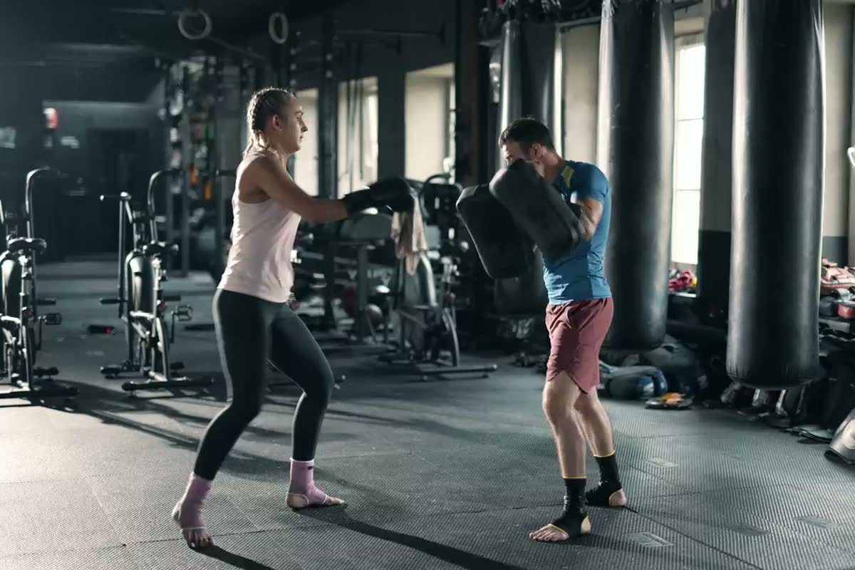 Un istruttore con i colpitori segue un’allieva di kickboxing in palestra