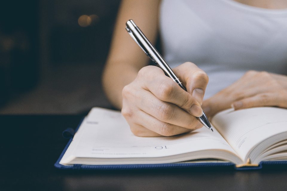 Una mano scrive con una penna su un’agenda aperta