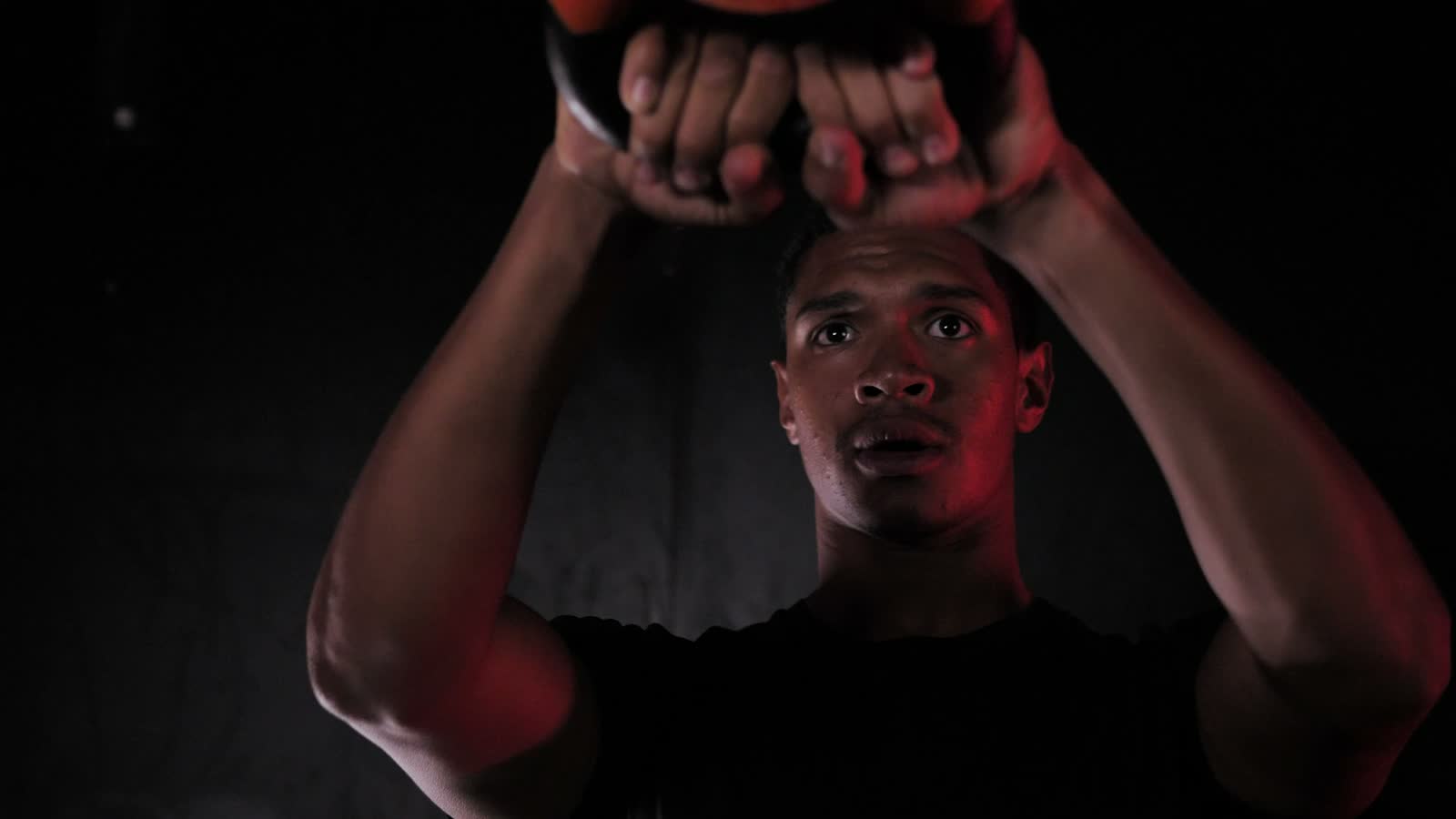 Un atleta solleva un kettlebell sopra la testa in un box illuminato di rosso