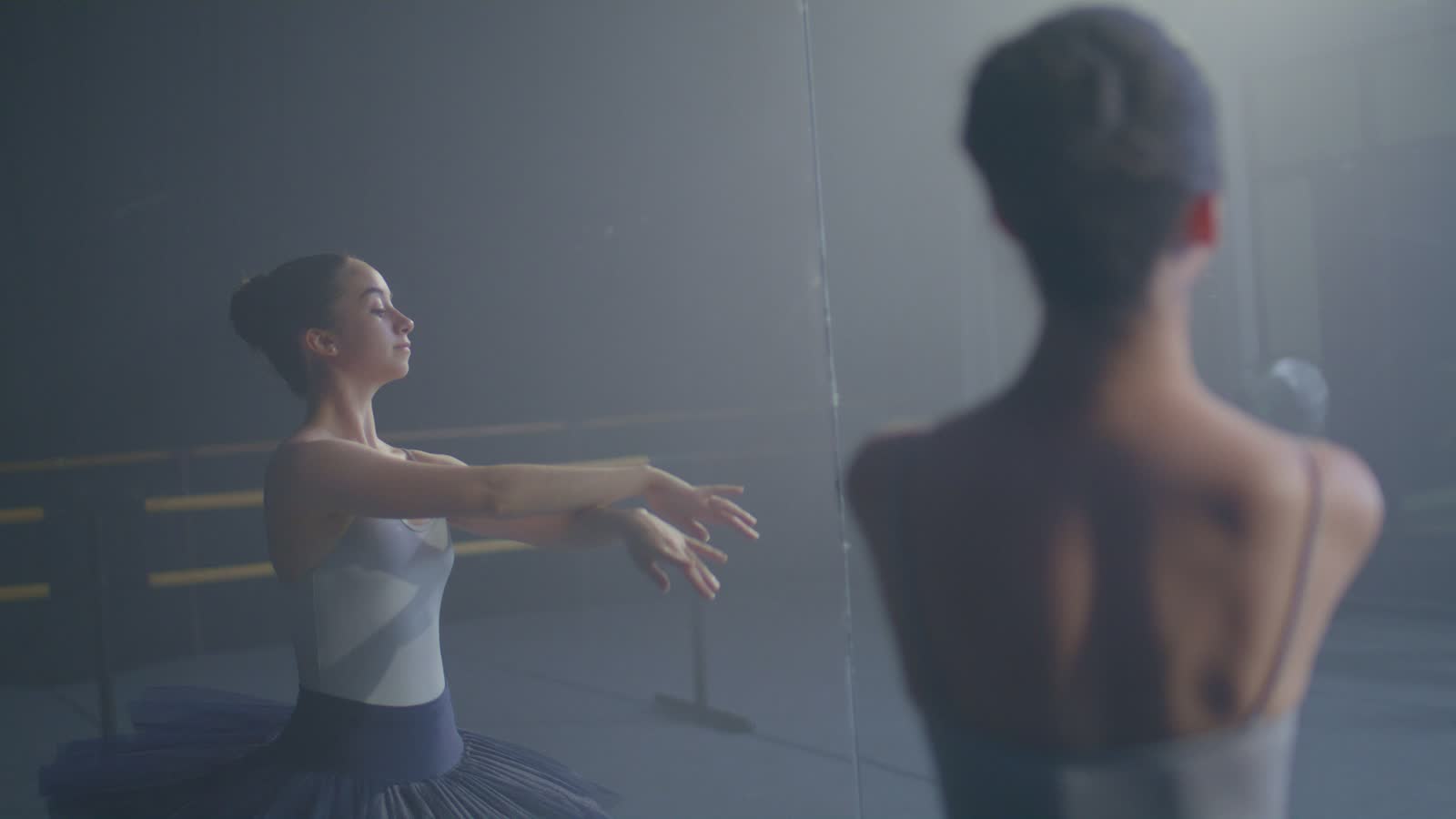 Una ballerina classica si allena alla sbarra davanti allo specchio in una sala luminosa
